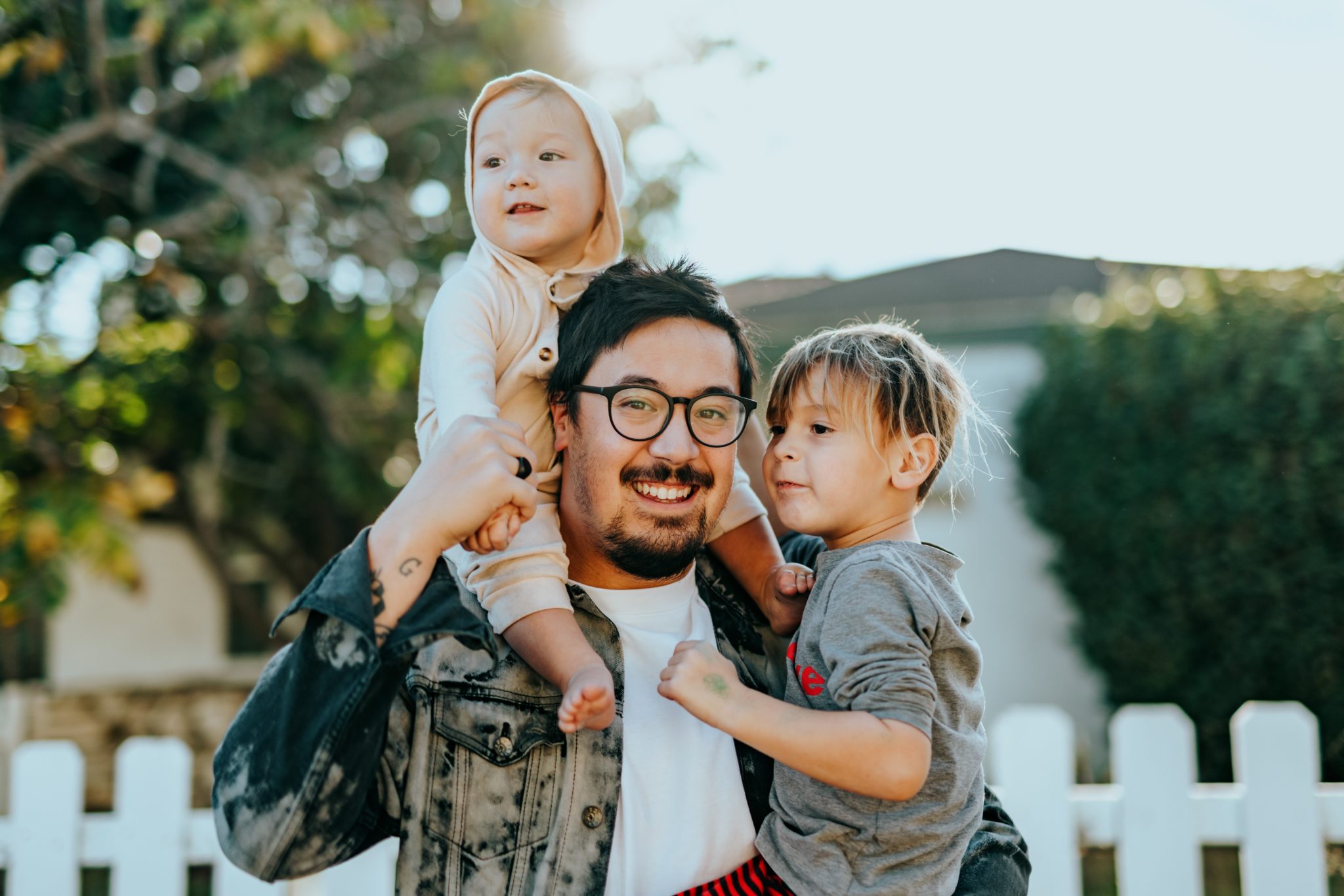 A parent carrying two young children outdoors